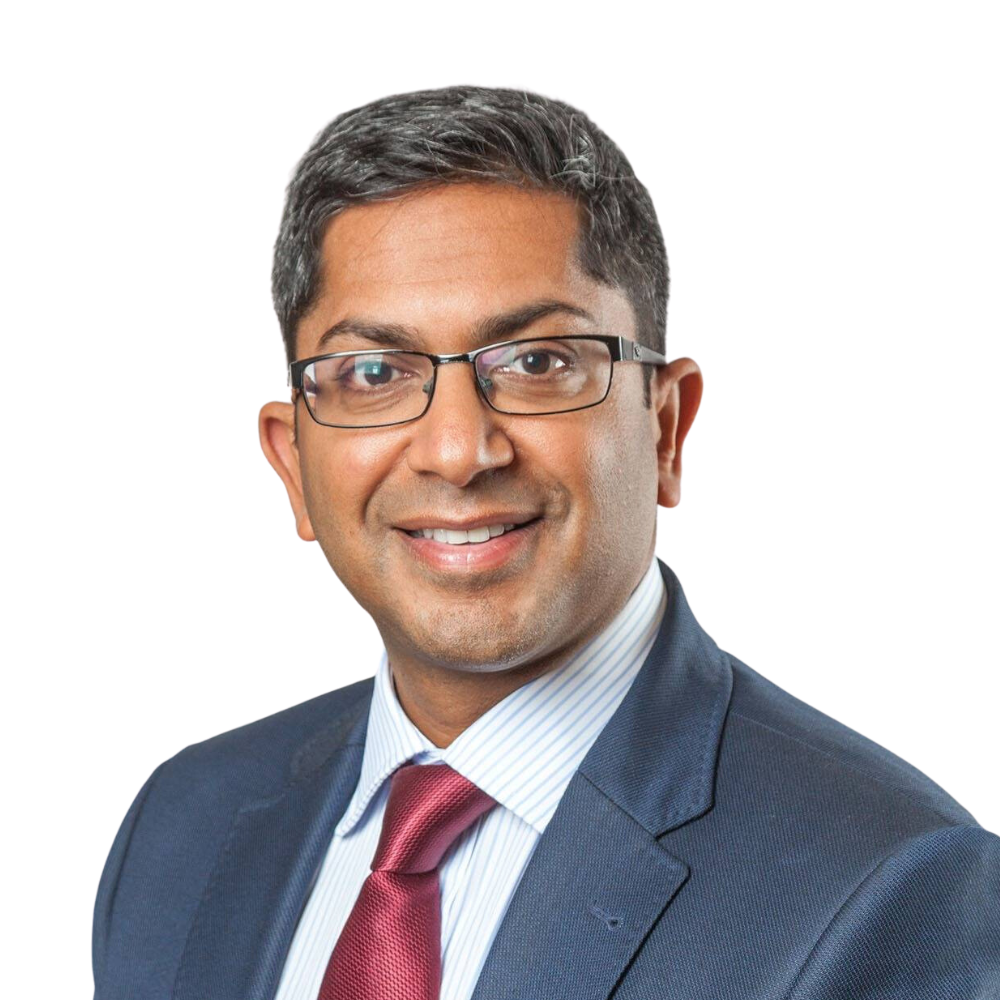 Mr Vasu Karri (Consultant Plastic Surgeon) in blue suit and red tie smiling at the camera